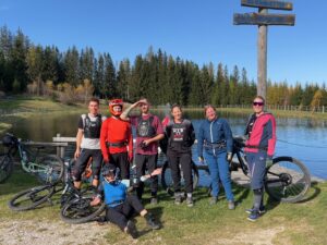 Eine gemischte Gruppe von Personen in Mountainbike-Kleidung steht vor einem Speicherteich